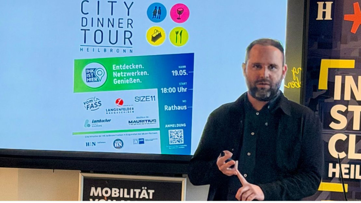 Moderne Präsentationssituation im Innenstadt-Club. Bastian Hiergeist aus der Wirtschaftsförderung präsentiert. Auf dem Bildschirm ist das Plakat der letzten City Dinner Tour zu erkennen.