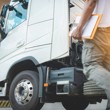 Ein Lkw steht auf einem Betriebsgelände. Daneben geht eine Person mit Klemmbrett am Fahrzeug entlang.