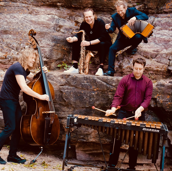 Das Bild zeigt vier Musiker mit ihren Instrumenten an einer Steinwand, es ist das Ensemble Quadro Nuevo.