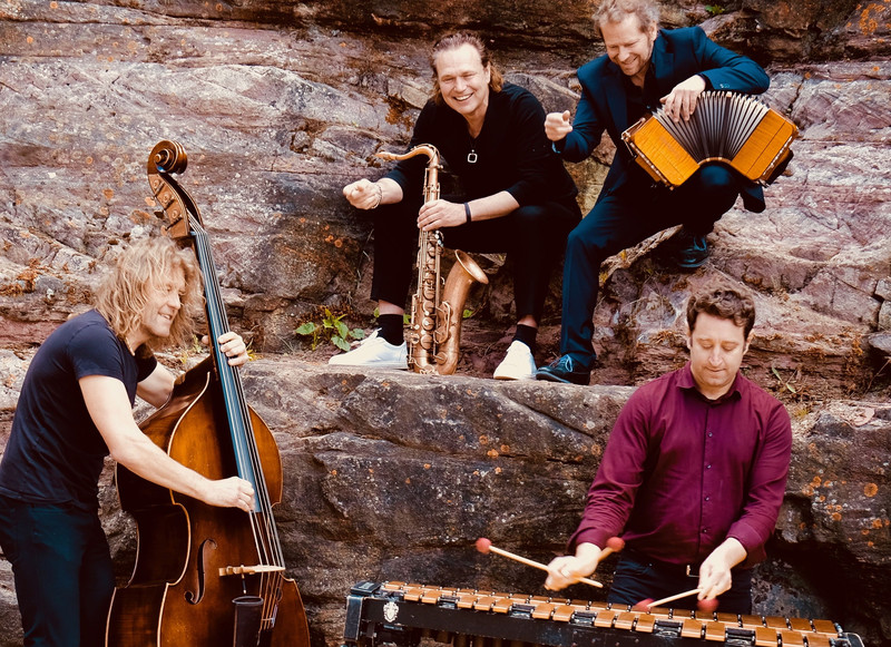 Das Bild zeigt vier Musiker mit ihren Instrumenten an einer Steinwand, es ist das Ensemble Quadro Nuevo.