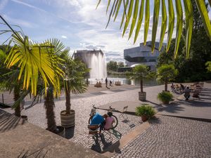 Neckarbühne (Fotograf: Christoph Düpper --- Bildnachweis: Heilbronn Marketing GmbH/Christoph Düpper) Menschen sitzen in der Sonne. Es stehen Palmen da. Sie sind am Neckar.