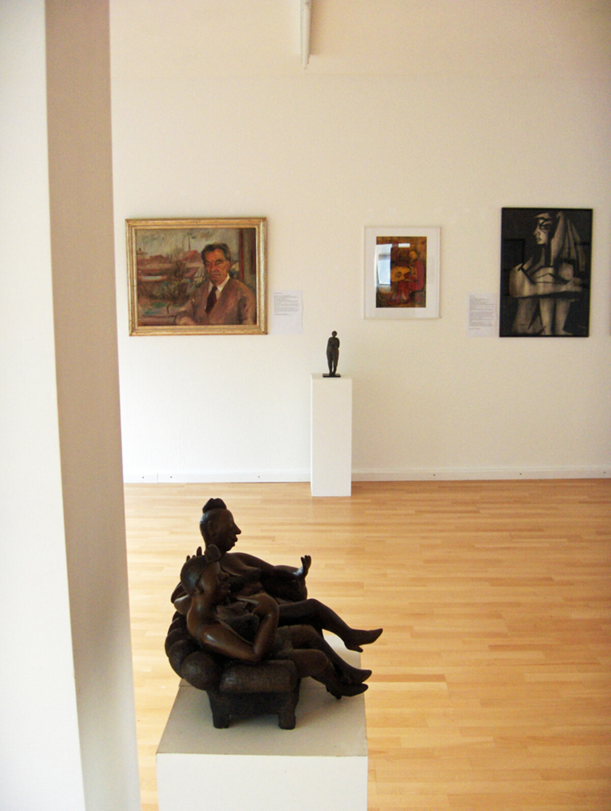Ausstellung 60 Jahre Künstlerbund 2009: Das Bild zeigt einen Ausstellungsraum des Künstlerbunds Heilbronn mit Werken aus den 60er Jahren. Im Vordergrund steht eine dunkle Skulptur auf einem Sockel. Dahinter sind an den weißen Wänden mehrere Gemälde zu sehen. Der Raum ist hell, mit Holzfußboden und klarer Präsentation der Kunstwerke. Die Szene vermittelt eine ruhige, konzentrierte Atmosphäre zur Betrachtung der Ausstellung.