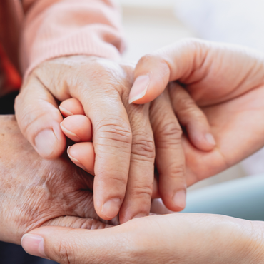 Eine jüngere Person hält behutsam die Hand einer älteren Person als Zeichen von Unterstützung und Fürsorge