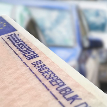 Ein deutscher Führerschein ist im Vordergrund zu sehen. Im unscharfen Hintergrund stehen mehrere Autos.