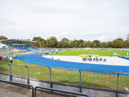 Das Bild zeigt das Frankenstadion in Heilbronn mit der blauen Laufbahn, dem Fußballrasen und der Tribüne. 