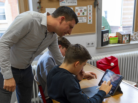 Das Bild zeigt einen Klassenraum im Robert-Mayer-Gymnasium. Ein Lehrer erklärt Neuntklässlern gerade, wie man ein i-Pad bedient. 