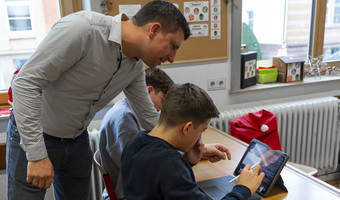 Das Bild zeigt einen Klassenraum im Robert-Mayer-Gymnasium. Ein Lehrer erklärt Neuntklässlern gerade, wie man ein i-Pad bedient. 