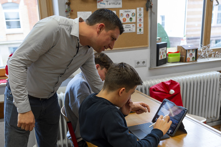 Das Bild zeigt einen Klassenraum im Robert-Mayer-Gymnasium. Ein Lehrer erklärt Neuntklässlern gerade, wie man ein i-Pad bedient. 