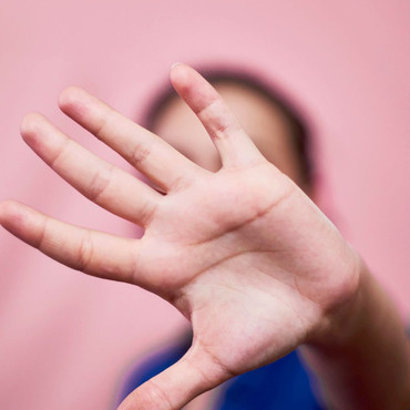 Eine ausgestreckte Hand verdeckt das Gesicht einer Person vor rosafarbenem Hintergrund.