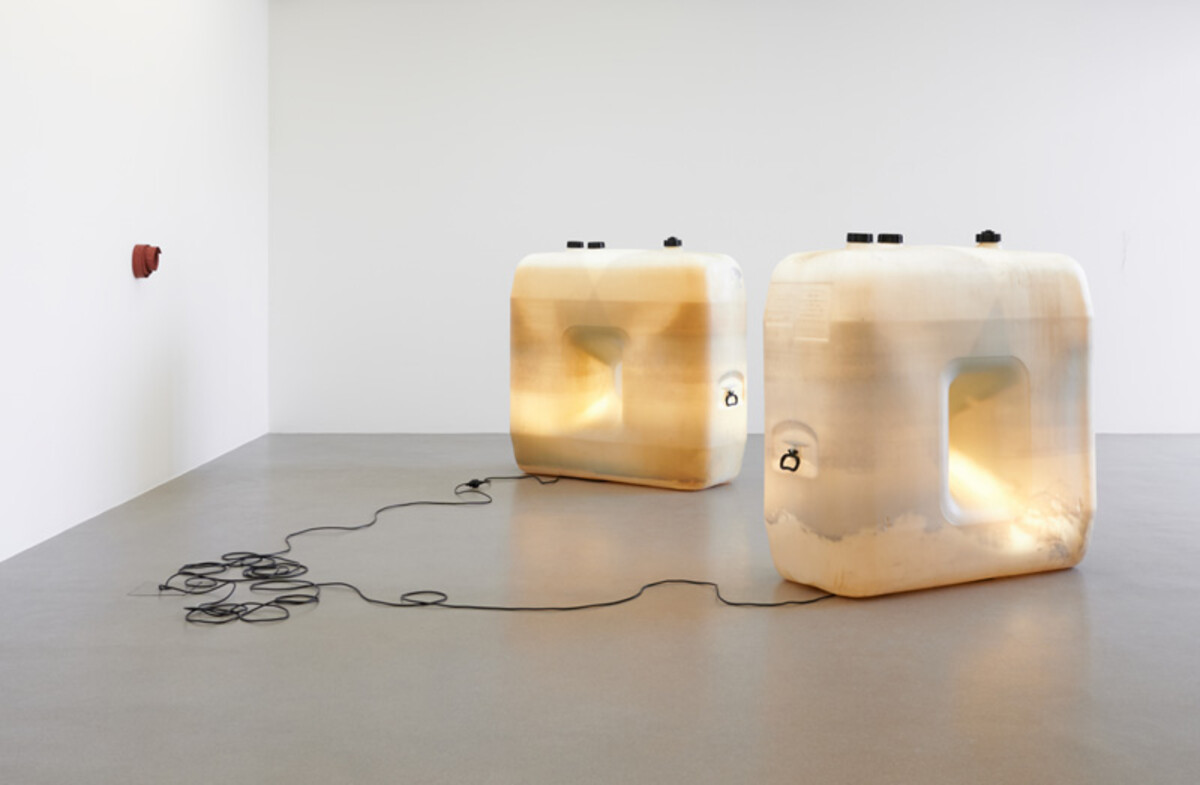 Das Bild zeigt eine Ausstellungssituation im Kunstverein Heilbronn. Auf dem Boden eines hellen, leeren Raumes stehen zwei große, leicht transparente Behälter mit weichen, abgerundeten Formen. Im Inneren sind Materialien erkennbar, die diffus beleuchtet wirken. Ein Kabel verbindet die Objekte miteinander und liegt locker auf dem Boden. Links an der Wand ist ein kleines weiteres Element angebracht. Die Arbeit stammt von Birgit Werres und war Teil einer Ausstellung im Jahr 2020. Birgit Werres, Ausstellungsansicht Kunstverein Heilbronn 2020 - Foto: Babette Bangemann, Düsseldorf