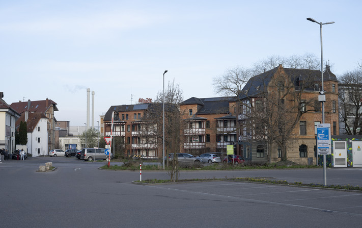 Das Bild zeigt einen großen Parkplatz in Vordergrund, der zu einem großen Lebensmittelmarkt gehört, der auf dem Areal des früheren Südbahnhofs entstand. Die Firma Knorr hat hier noch ihren Sitz. Die Wohngebäude sind erhalten geblieben und modernisiert worden. Autos haben verstärkt den öffentlichen Raum erobert.