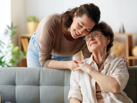 Das Bild zeigt eine junge Betreuerin, die eine Seniorin in deren Wohnung in dem Arm nimmt.