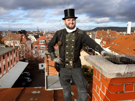 Das Bild zeigt einen Schornsteinfeger auf einem Dach in der Stadt Heilbronn. 