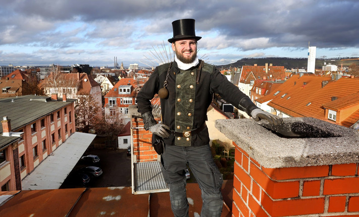 Das Bild zeigt einen Schornsteinfeger auf einem Dach in der Stadt Heilbronn. 