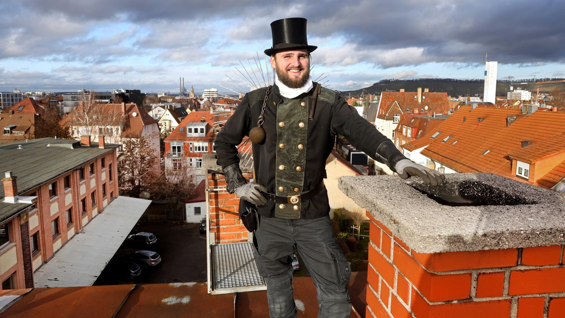 Das Bild zeigt einen Schornsteinfeger auf einem Dach in der Stadt Heilbronn. 