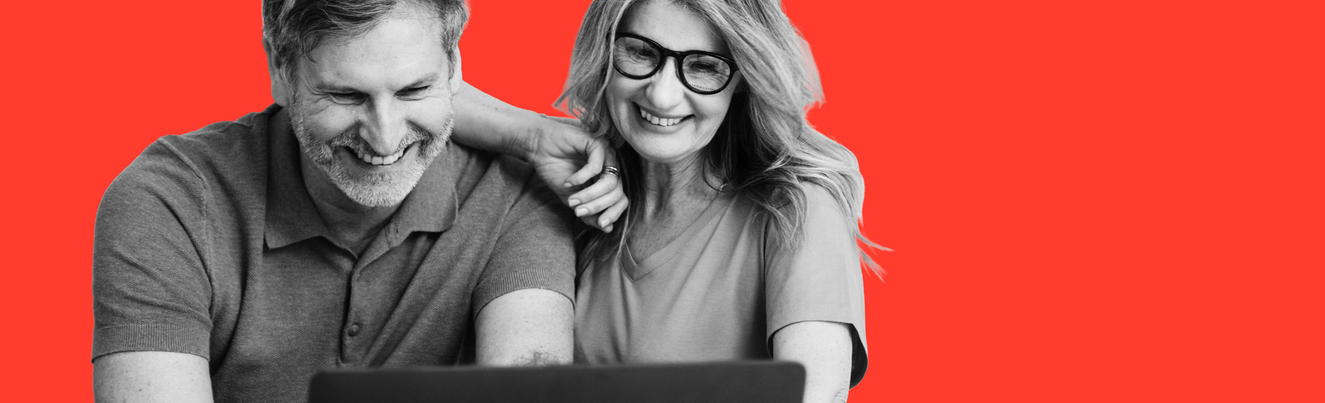 Symbolbild: Ein lächelnder Mann und eine lächelnde Frau schauen gemeinsam auf einen Laptop vor rotem Hintergrund.