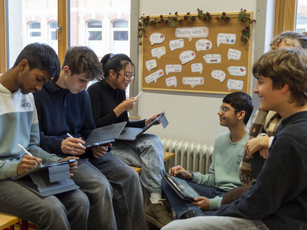 Das Bild zeigt Schülerinnen und Schüler des Robert-Mayer-Gymnasiums in einem Klassenraum, die ihre neuen Tablets ausprobieren. 
