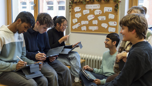 Das Bild zeigt Schülerinnen und Schüler des Robert-Mayer-Gymnasiums in einem Klassenraum, die ihre neuen Tablets ausprobieren. 