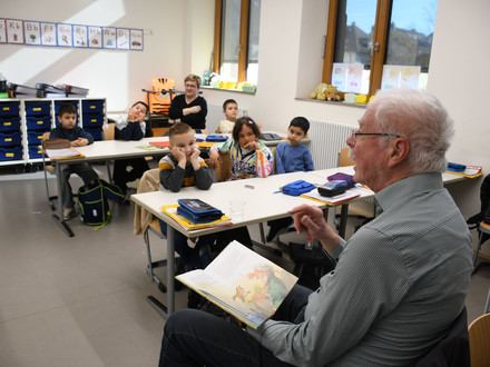 Das Bild zeigt einen Vorlesepaten in der Dammgrundschule, der Mädchen und Jungen einer Sprachklasse aus dem Märchen "Die Bremer Stadtmusikanten" vorliest. 