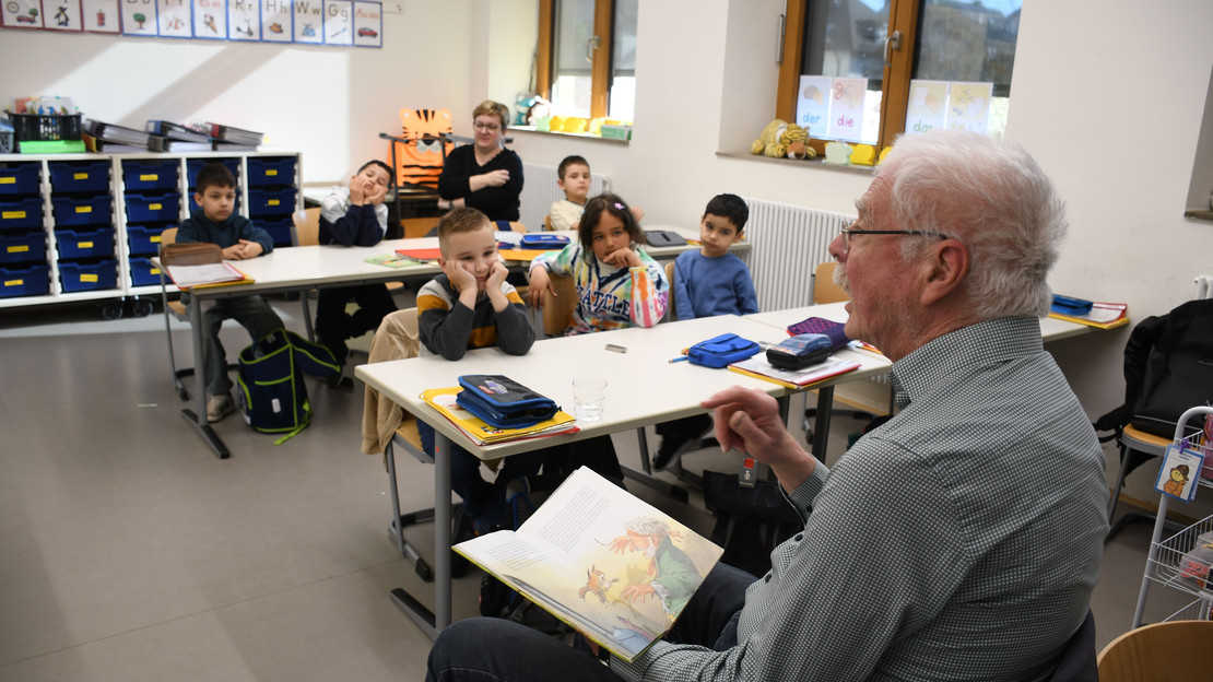 Das Bild zeigt einen Vorlesepaten in der Dammgrundschule, der Mädchen und Jungen einer Sprachklasse aus dem Märchen "Die Bremer Stadtmusikanten" vorliest.