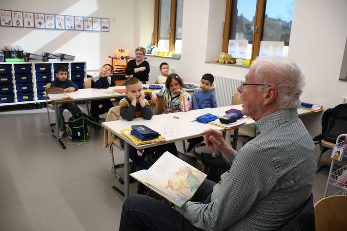 Das Bild zeigt einen Vorlesepaten in der Dammgrundschule, der Mädchen und Jungen einer Sprachklasse aus dem Märchen "Die Bremer Stadtmusikanten" vorliest.