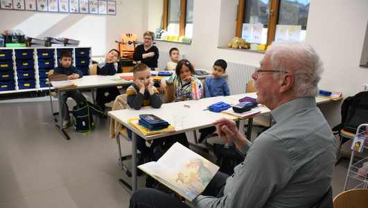 Das Bild zeigt einen Vorlesepaten in der Dammgrundschule, der Mädchen und Jungen einer Sprachklasse aus dem Märchen "Die Bremer Stadtmusikanten" vorliest. 