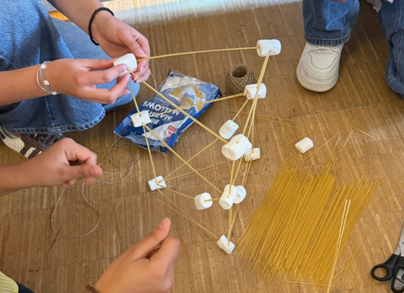 Mehrere Nachwuchskräfte bauen bei einer gemeinsamen Aufgabe eine Konstruktion aus Spaghetti, Marshmallows und Schnur.
