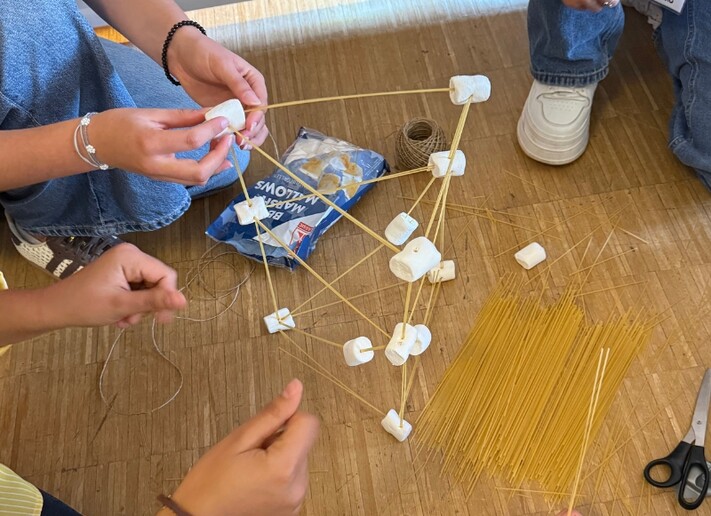 Mehrere Nachwuchskräfte bauen bei einer gemeinsamen Aufgabe eine Konstruktion aus Spaghetti, Marshmallows und Schnur.