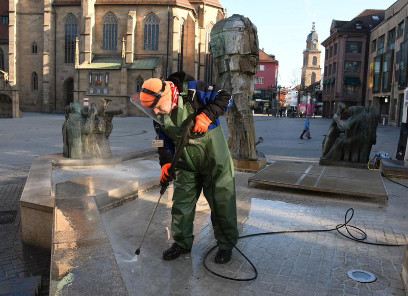 Das Bild zeigt einen Mitarbeiter des Betriebsamtes in Wathose und Schutzhelm,wie er per Dampstrahl den Komödiantenbrunnen vor dem Osterfest reinigt.