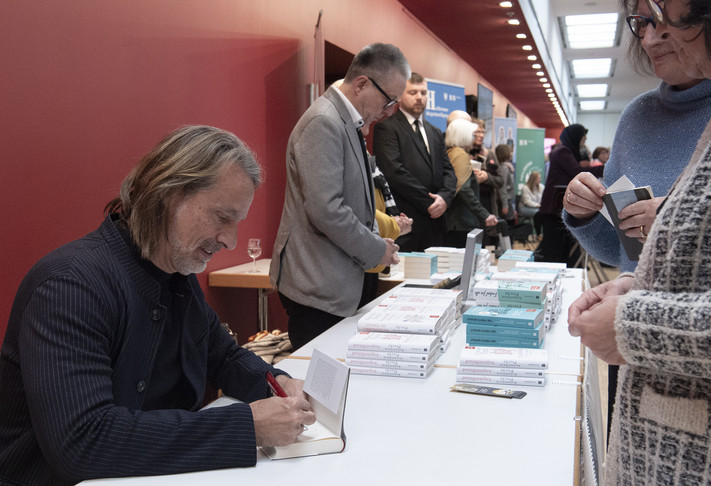 Das Bild zeigt Autor Richard David Precht beim Signieren seiner Bücher. 