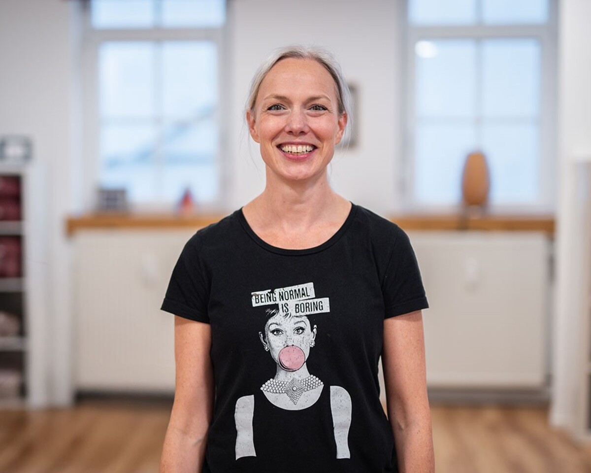 Eine Frau mit grauen Haaren, die lächelt. Sie trägt ein schwarzes T-Shirt mit der Aufschrift "Being normal is boring"