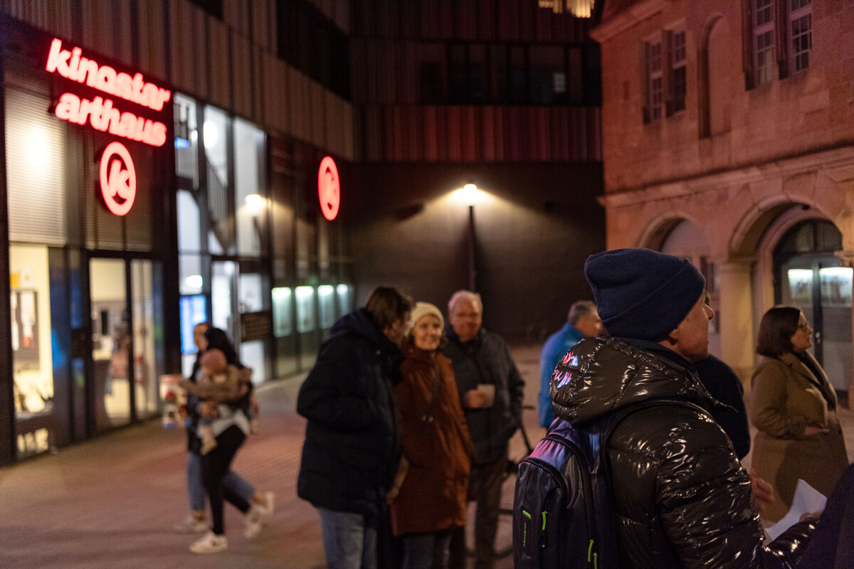 Menschen stehen auf der Straße vor einer Reklamebeleuchtung