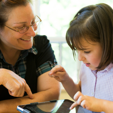Kind und erwachsene Person nutzen gemeinsam ein Tablet und tippen auf den Bildschirm