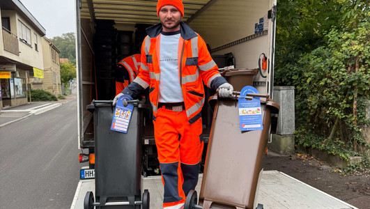 Das Bild zeigt einen Mitarbeiter einer Entsorgungsfirma, der die neuen Restmüll-  und Biotonnen mit integriertem Chip ausliefert. 