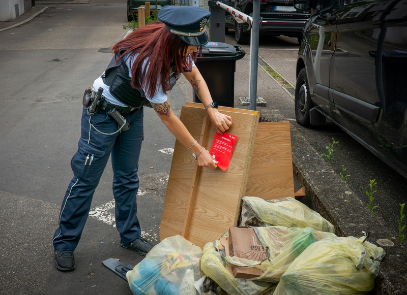 Das Bild zeigt ein Waste-Watcher-Mitglied, das einen roten Hinweiszettel an eine illegale Müllablagerung klebt. Dies soll klar machen, dass das wilde Abstellen illegal ist. 