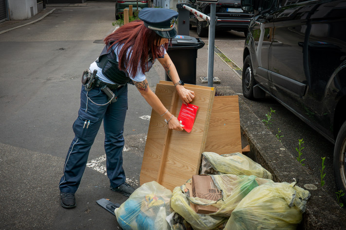 Das Bild zeigt ein Waste-Watcher-Mitglied, das einen roten Hinweiszettel an eine illegale Müllablagerung klebt. Dies soll klar machen, dass das wilde Abstellen illegal ist.
