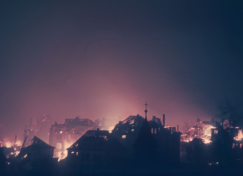 Das Bild vom Bombenabend 1944 zeigt Häusersilhouetten, die durch das ausgelöste Feuer der vielen Bomben erleuchtet sind. 