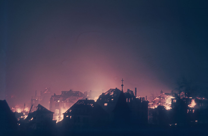 Das Bild vom Bombenabend 1944 zeigt Häusersilhouetten, die durch das ausgelöste Feuer der vielen Bomben erleuchtet sind. 