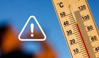 Nahaufnahme eines Thermometers mit hoher Temperaturanzeige vor blauem Himmel. Ein weißes Warnsymbol mit Ausrufezeichen weist auf die gesundheitlichen Risiken großer Hitze hin.