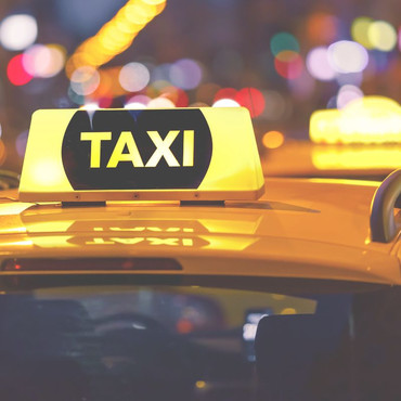 Das Dach eines Taxis mit dem gelb leuchtenden Schild. Im Hintergrund ist verschwommen eine Stadt zu erkennen.