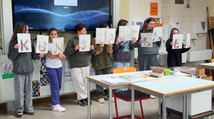 Foto einer Gruppe Schülerinnen und Schüler der Dammrealschule. Sie stehen im Kunst Klassenzimmer und halten selbstgestaltete Papiere mit Buchstaben hoch, die das Wort Kunstatelier ergeben.