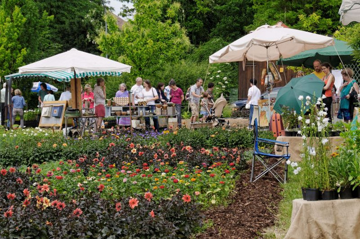 Das Bild zeigt Verkaufsstände mit Schirmen und interessierte Menschen im Obstgarten.