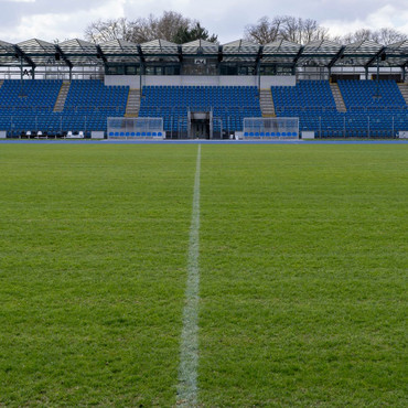 Blick über den Rasen und die Mittellinie auf die leere Haupttribüne des Frankenstadions mit blauen Sitzreihen.