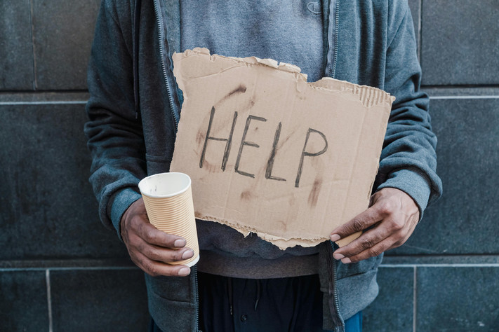 Das Bild zeigt einen Menschen in einfacher Kleidung, der ein Schild mit dem Wort "Help" für "Hilfe in den Händen hält. 