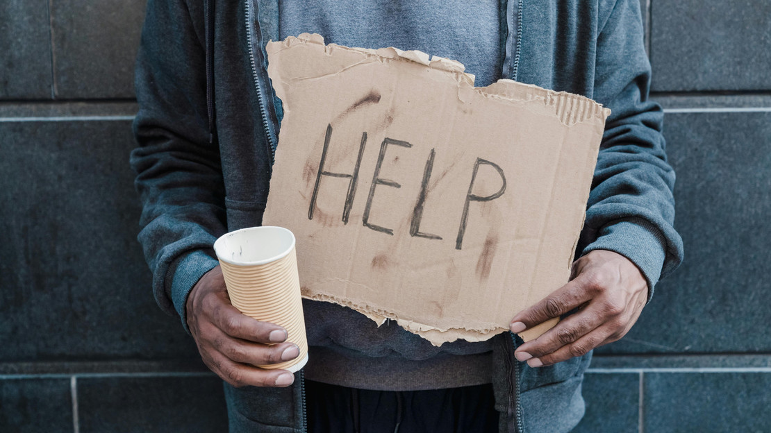 Das Bild zeigt einen Menschen in einfacher Kleidung, der ein Schild mit dem Wort "Help" für "Hilfe in den Händen hält. 