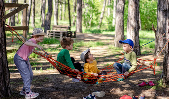 Das Bild zeigt spielende Kinder in einer Hängematte zwischen Bäumen. Es thematisiert das breite Angebot des Sommerferienprogramms. 