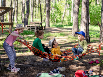 Das Bild zeigt spielende Kinder in einer Hängematte zwischen Bäumen. Es thematisiert das breite Angebot des Sommerferienprogramms.