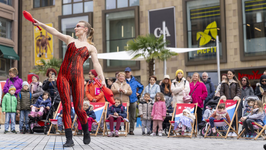 Das Bild zeigt eine Frau in rotem Kostüm auf dem Kiliansplatz, die am Kultursamstag mit Keulen jongliert und Passantinnen und Passanten unterhält. 