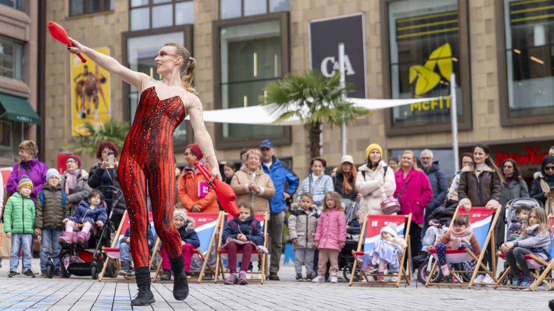 Das Bild zeigt eine Frau in rotem Kostüm auf dem Kiliansplatz, die am Kultursamstag mit Keulen jongliert und Passantinnen und Passanten unterhält. 