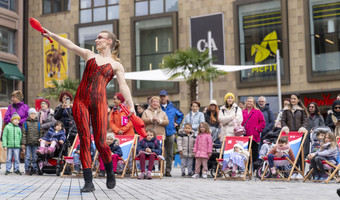 Das Bild zeigt eine Frau in rotem Kostüm auf dem Kiliansplatz, die am Kultursamstag mit Keulen jongliert und Passantinnen und Passanten unterhält. 